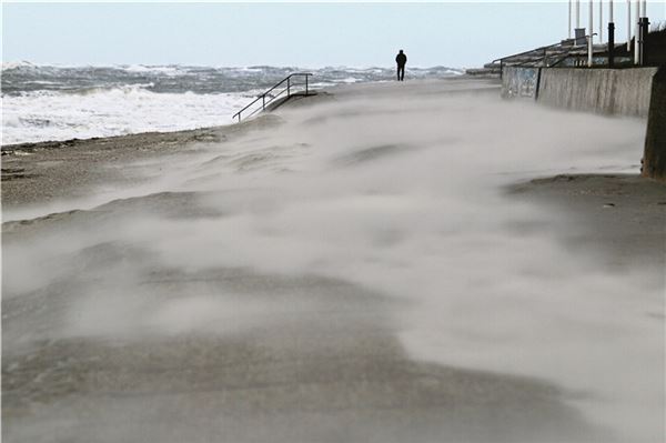 Sturm schäumt Wellen der Nordsee auf Der Wind bläst Sand über die Promenade.