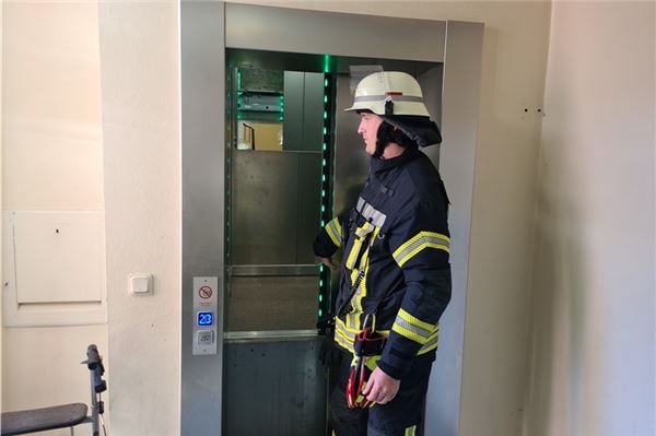Ein Feuerwehrmann sichert die Tür des Fahrstuhls in dem Norder Mehrfamilienhaus. Dort steckte eine Familie fest.
