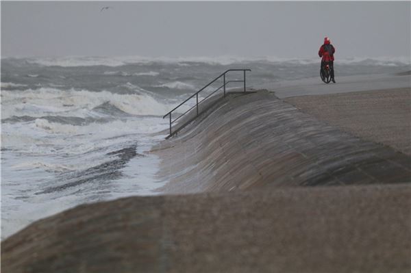 Eine Radfahrerin steht bei stürmischem Wetter an der Wasserkante auf Norderney. Ein Tiefausläufer sorgte am Mittwoch für stürmisches Wetter im Norden.