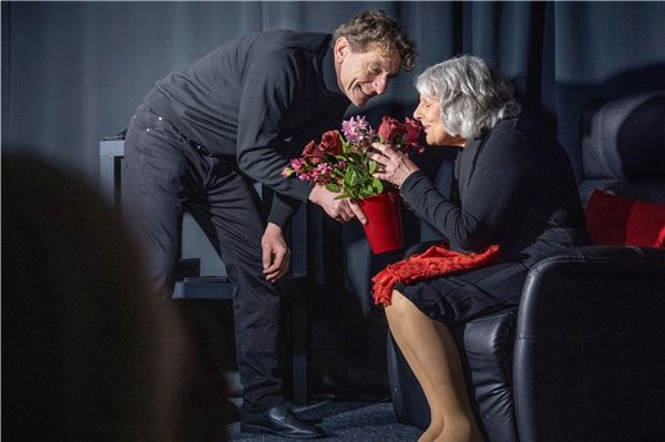 Der Sohn (Peter Spetzke) überreicht seiner Mutter Blumen zum 77. Geburtstag.