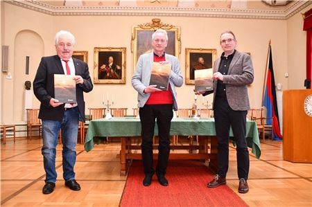 Dr. Rolf Bärenfänger (Mitte) freut sich über die Festschrift, die Kollegen und Wegbereiter für ihn geschrieben haben. Überreicht wurde sie von Dr. Jan Kegler (r.), Abteilungsleiter Archäologie, und Landschaftspräsident Rico Mecklenburg.