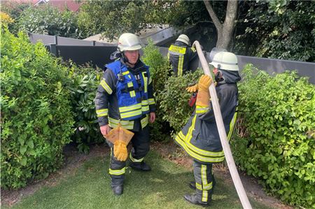 Drei Feuerwehrmänner führen Nachlöscharbeiten im Garten durch.