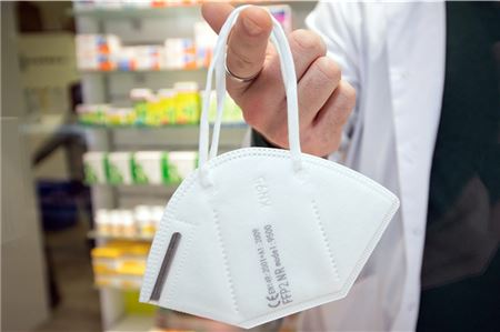 Ein Apotheker hält eine FFP2-Maske an einem Finger. In der Öffentlichkeit ist das Tragen Pflicht, am häufigsten stecken sich Infizierte jedoch in der Familie an.