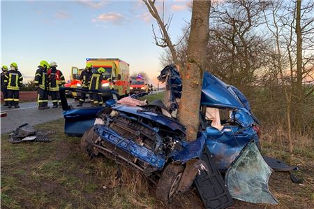 Feuerwehrleute stehen hinter einem völlig zerstörten Fahrzeug. Ein 21-Jähriger ist am ersten Weihnachtstag in Osteel von der Straße abgekommen, gegen einen Baum geprallt und tödlich verletzt worden.