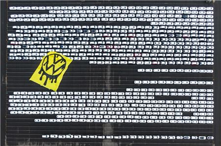 Greenpeace-Aktivisten breiten ein riesiges Protesttransparent über Autos aus, die auf dem Verladeplatz von VW stehen (Aufnahme mit Drohne).