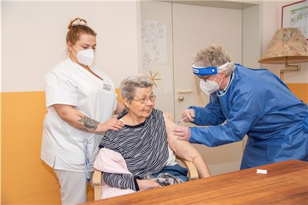 Renate Drees setzt bei Karin Kaminski die Nadel an. Die 80-Jährige wurde gestern im Helenen-stift in Hage als erste Person im Landkreis Aurich geimpft. Ihr zur Seite steht Pflegekraft Michaela Niebling. Foto: Ulferts