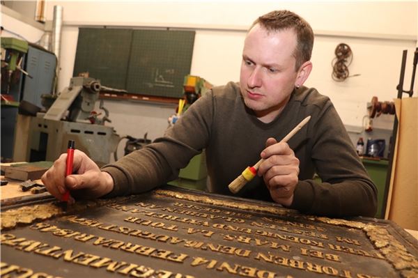 Zu neuem Glanz verhelfen: Keno Claassen reinigt die Gedenktafel vorsichtig von Farbresten und Schmutz. Im Anschluss wird das Stück mit einem mikrokristallinen Wachs konserviert.